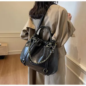Model wearing a vintage black pleated PU leather tote bag with gold chain and beige trench coat