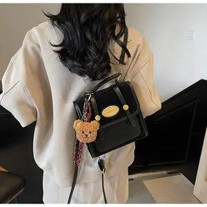 Détail du sac bandoulière noir avec logo en métal doré et breloque ours en peluche