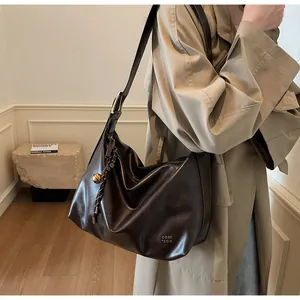 Détail du sac cabas en cuir marron foncé avec breloque métallique tissée et boucle dorée
