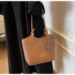 Detail of tan lychee grain tote bag with flower charm and metallic fashion brand plate