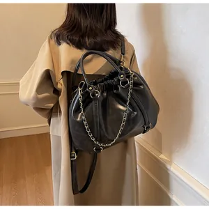 Detail of black pleated PU leather tote bag with gold chain strap on shoulder