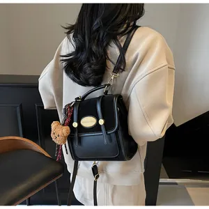 Détail d'un sac à dos multifonctionnel en cuir noir avec plaque dorée et breloque ours