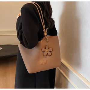 Brown lychee leather tote bag with flower charm shown on model in warm lighting