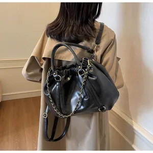 Detailed view of a black pleated drawstring bag with chain straps on a khaki trench coat