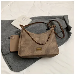 Close-up of retro suede crossbody bag with fashion label and metal chain detail on coat