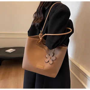 Detail of camel bucket bag showing textured lychee grain leather and flower pendant charm