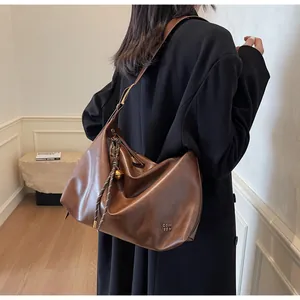 Détail d'un sac cabas en cuir brillant marron foncé avec logo et pendentif boule dorée