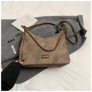 Macro shot of retro brown faux suede hobo bag with gold metal logo and chain strap