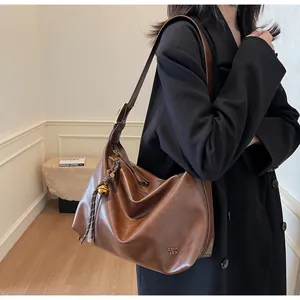Détail du sac cabas en cuir marron avec logo en métal doré et pendentif cloche tressé