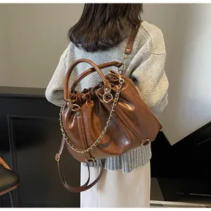 Detail of vintage brown PU leather bucket bag with pleated texture and golden chain strap