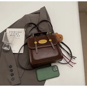 Sac à dos en cuir marron foncé avec boucle dorée et pendentif ours en peluche