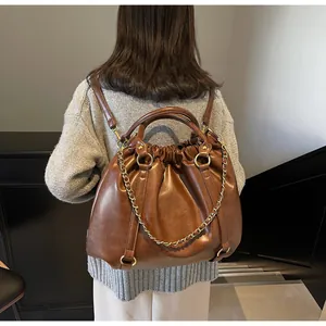 Detail of dark brown vintage pleated PU leather backpack with gold chain on model