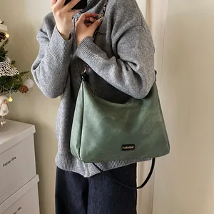Dark green faux suede tote bag with slim black straps and fashion label in daily setting