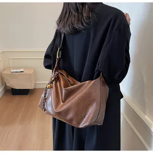 Détail du grand sac cabas marron montrant le pompon en corde tressée et le logo en métal doré