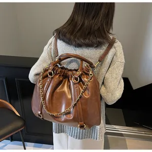 Detail view of dark brown pleated leather backpack with golden chain and shoulder straps