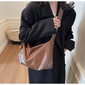 Détail du sac hobo en cuir marron vintage avec logo doré et pendentif sphérique