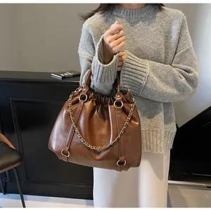 Close-up of brown pleated PU leather handbag with decorative chunky gold chain detail