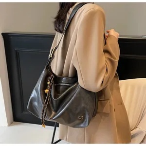 Détail du grand cabas gris foncé brillant avec logo doré et large bandoulière sur modèle