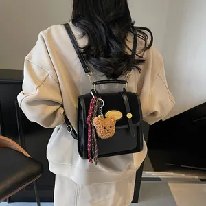 Sac à dos noir bi-matière avec boucles dorées et porte-clé ours en peluche sur le dos