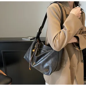 Détail du sac hobo noir brillant avec boucle dorée et pendentif tissé élégant