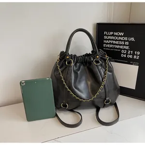 Detail of black pleated faux leather handbag featuring gold chain and metallic buckle
