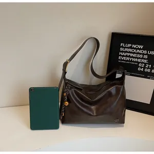 Détail du sac cabas marron brillant avec boucle dorée et breloque tissée décorative