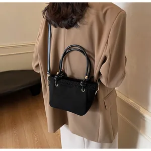 Detail of black crossbody bucket bag featuring faux shearling trim and knotted top handles
