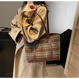 Detail of checkered tote bag with brown leather handles worn by a model in a trench coat