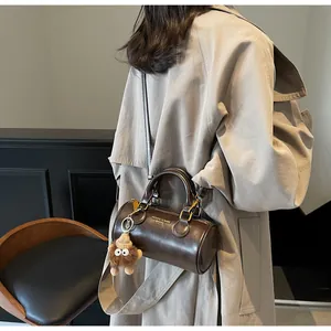 Detail of a dark brown cylindrical crossbody bag with gold hardware and plush charm