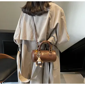 Detail of a brown cylindrical mini bag with plush eye charm on a stylish trench coat