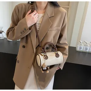 Detail view of beige mini barrel crossbody bag with fashion slogan and monkey charm