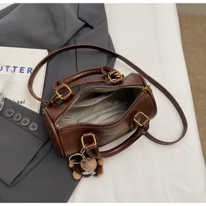 Detailed view of deep brown cylinder boston bag on grey suit with plush doll charm