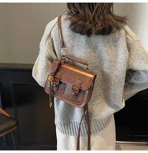 Detail of vintage brown leather satchel featuring double front pockets and bell charm
