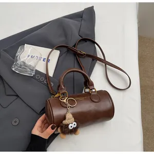 Detail of dark brown cylindrical handbag with oil-wax texture and plush doll charm