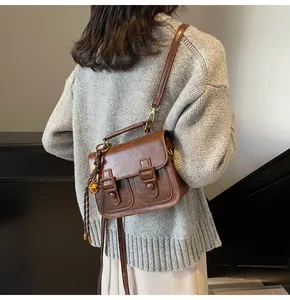 Close-up of vintage brown satchel with golden bell charm worn by model in gray knitwear