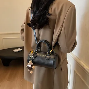 Retro black cylindrical crossbody bag with gold lettering and brown plush monster charm