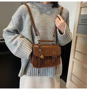 Close-up of vintage brown crossbody bag worn with a knitted sweater and accessories