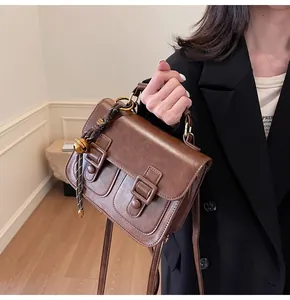 Detail of vintage brown leather satchel with dual buckle design and decorative bell charm