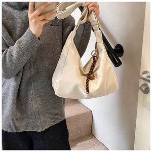 Detail of a beige leather hobo bag with brown braided rope and gold ring accents