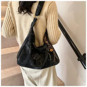 Close-up of a black glossy hobo bag with a side knot detail and wide shoulder strap
