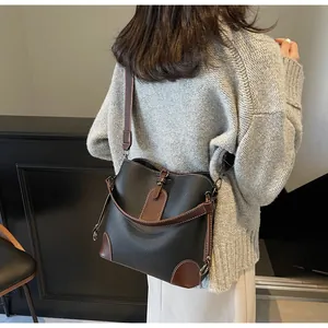 Detail of black bucket bag with brown leather trim and contrast white stitching on a model