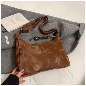Detail of a brown glossy leather crescent bag with a decorative woven rope knot accessory