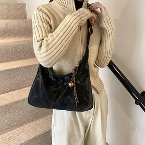 Elegant black hobo shoulder bag with golden bell charm and woven strap on a model