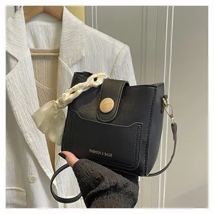 Detail of black leather bucket bag featuring a wooden buckle and silk scarf handle