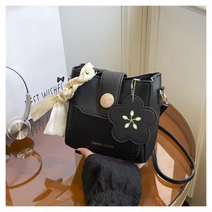 Detailed close-up of a black leather bucket bag with silk scarf and floral pendant charm