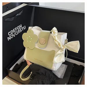 Detail of white and green bucket bag featuring floral charm and silk wrapped handle