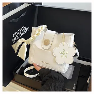 Detail of white leather handbag featuring silk scarf handle and floral charm accessory