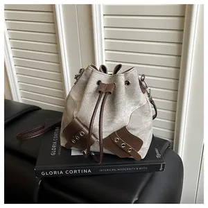 Detail view of canvas bucket bag with brown leather trim, drawstring, and silver eyelets