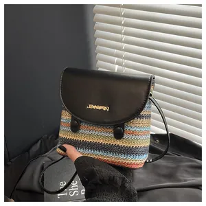 Detail of colorful woven straw bucket bag featuring black leather lid with gold logo