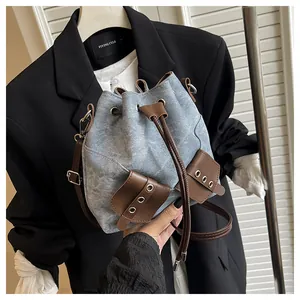 Detail of light blue denim bucket bag with brown leather drawstrings and adjustable strap